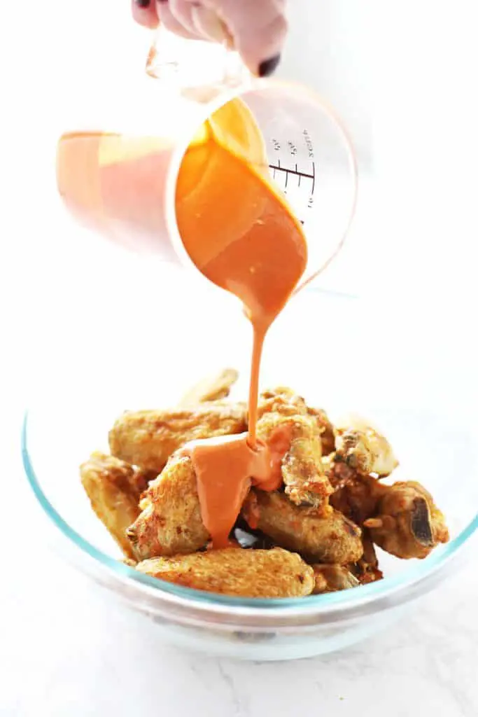 Buffalo sauce being poured on air fryer chicken wings.