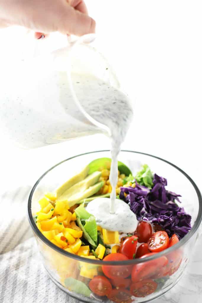 Healthy ranch dressing being poured on salad.