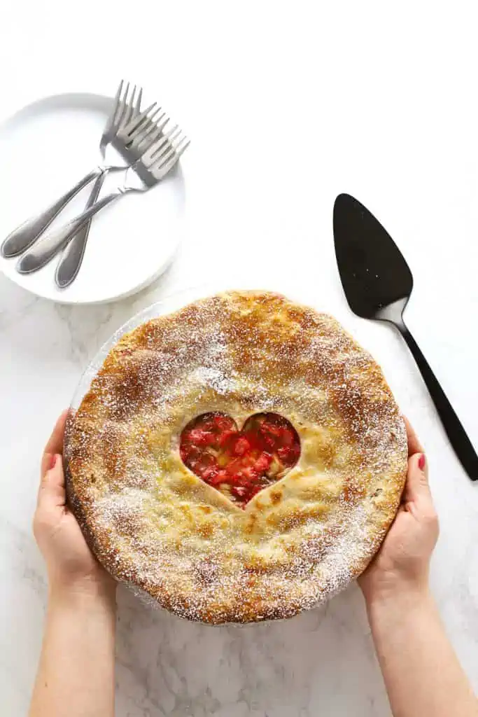 Two hands holding a strawberry rhubarb pie. 