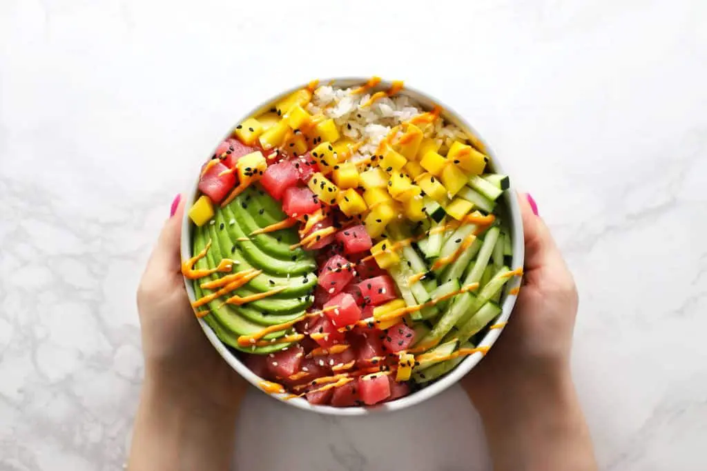 Two hands holding tuna poke sushi bowl.