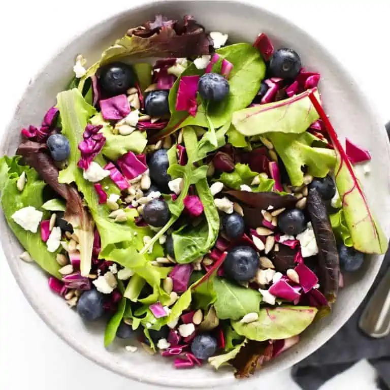 Blueberry goat cheese salad in grey bowl with fork and blue napkin.