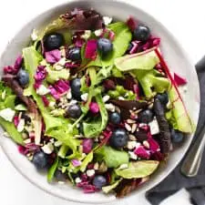 Blueberry goat cheese salad in grey bowl with fork and blue napkin.