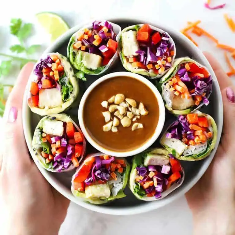 Two hands holding white bowl with summer rolls and peanut sauce.