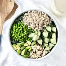 Green grain summer salad in white bowl with wood serving utensils.