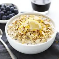 Lemon poppy seed overnight oats in a white bowl with blueberries and coffee.