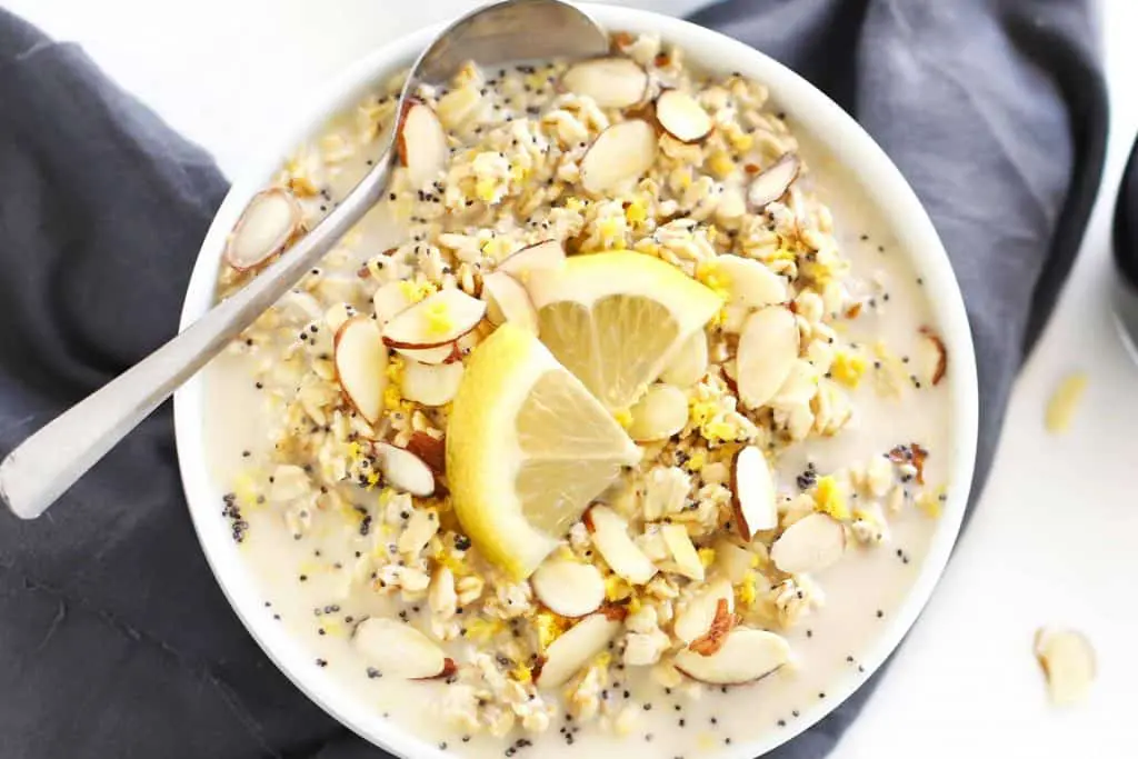 Lemon poppy seed overnight oats in a white bowl with lemon wedges.