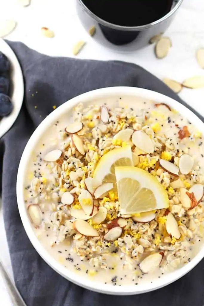 Lemon poppy seed overnight oats in a white bowl with lemon wedges and grey napkin.