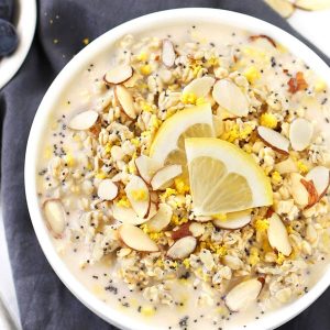 Lemon poppy seed overnight oats in a white bowl with lemon wedges and grey napkin.
