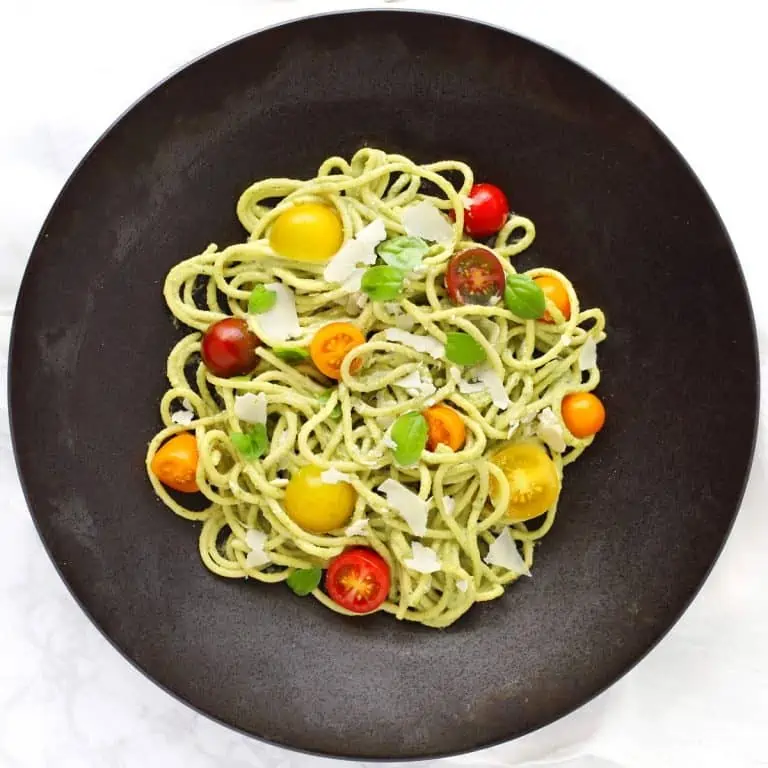 Creamy basil cashew pasta with tomatoes in black bowl.