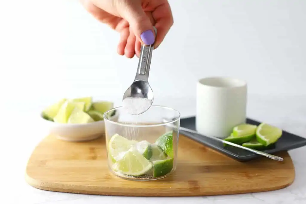 Pouring sugar over limes in a glass.