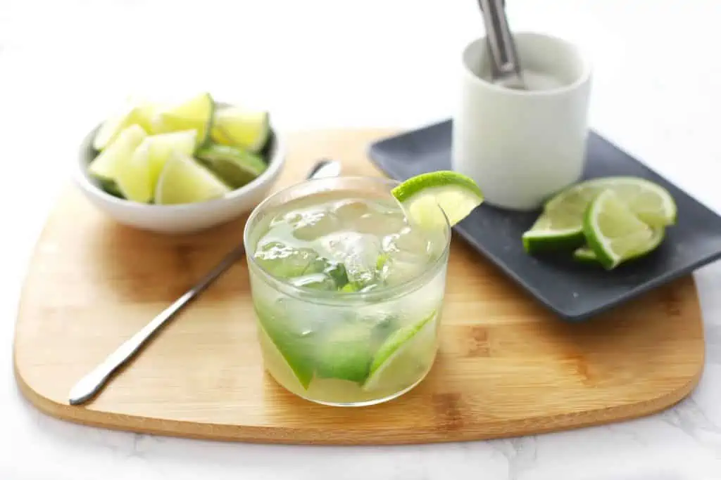 Caipirinha in glass on cutting board with limes and sugar.