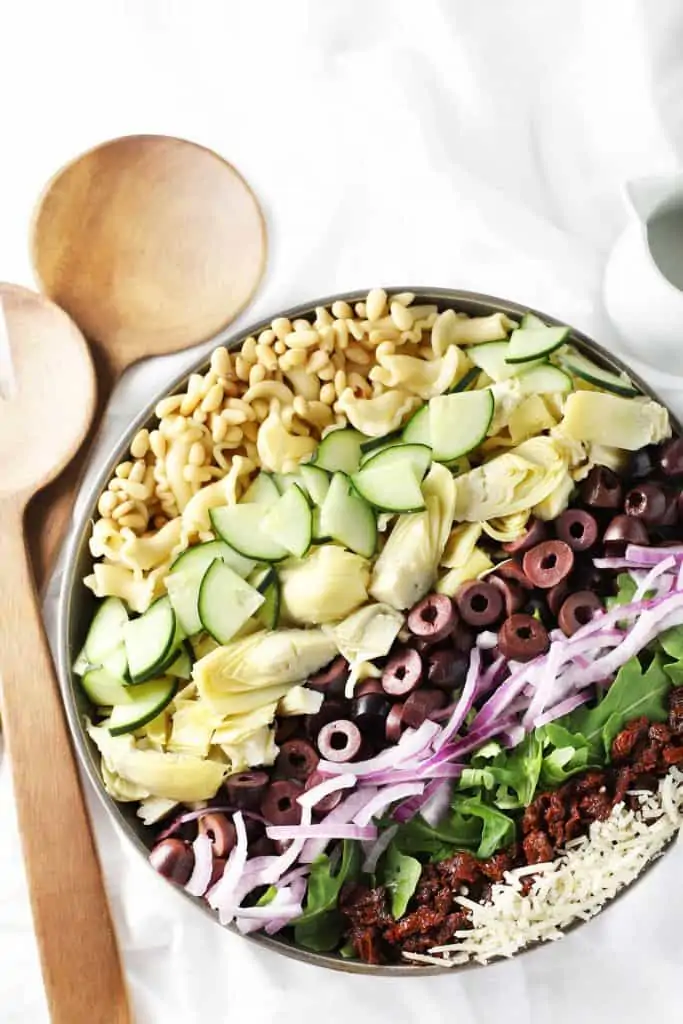 Mediterranean pasta salad in grey bowl with serving utensils.