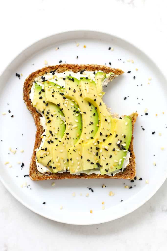 Everything bagel avocado toast with a bite taken out of it on a white plate.