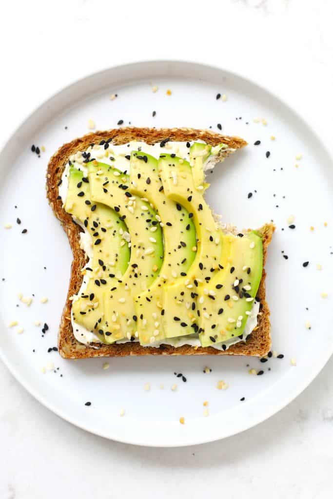 Everything bagel avocado toast with a bite taken out of it on a white plate. 