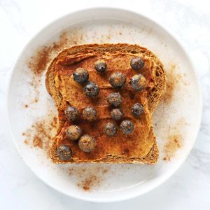 Peanut butter blueberry toast on white plate with cinnamon.