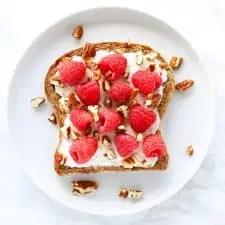 Raspberry cream cheese toast with pecans on white plate.
