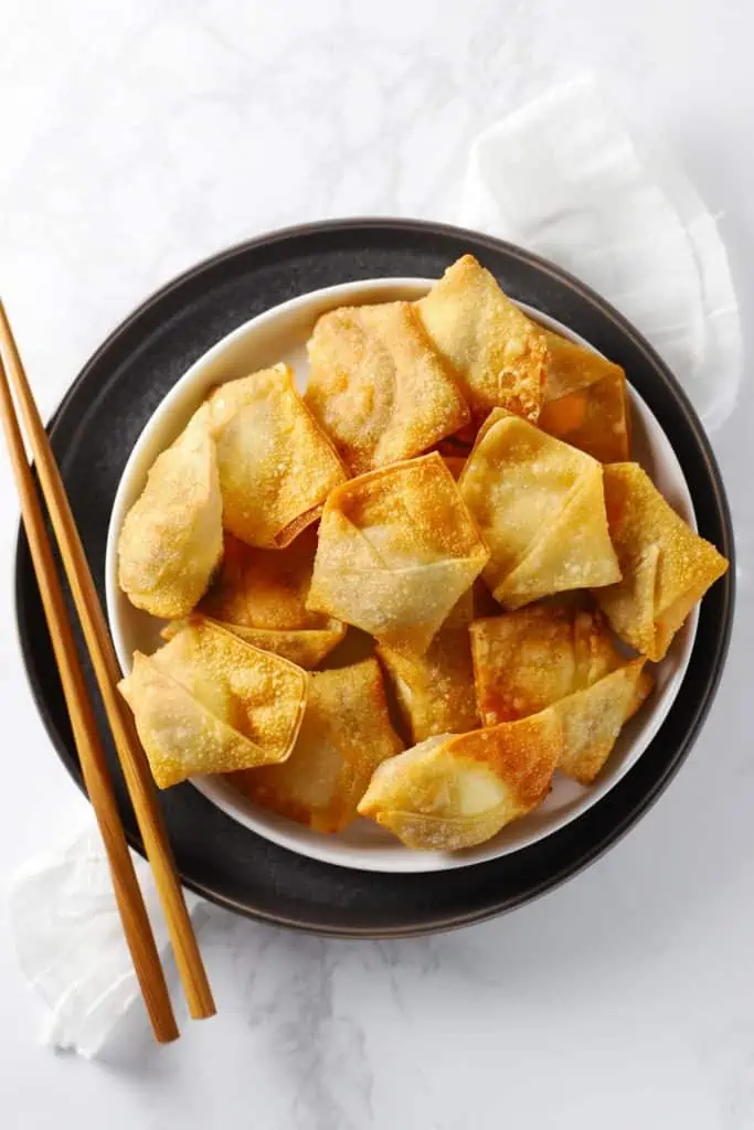 Cream cheese wontons on grey plate with chopsticks.