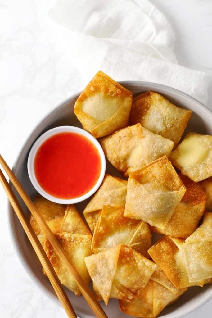 Cream cheese wontons on white plate with dipping sauce. 