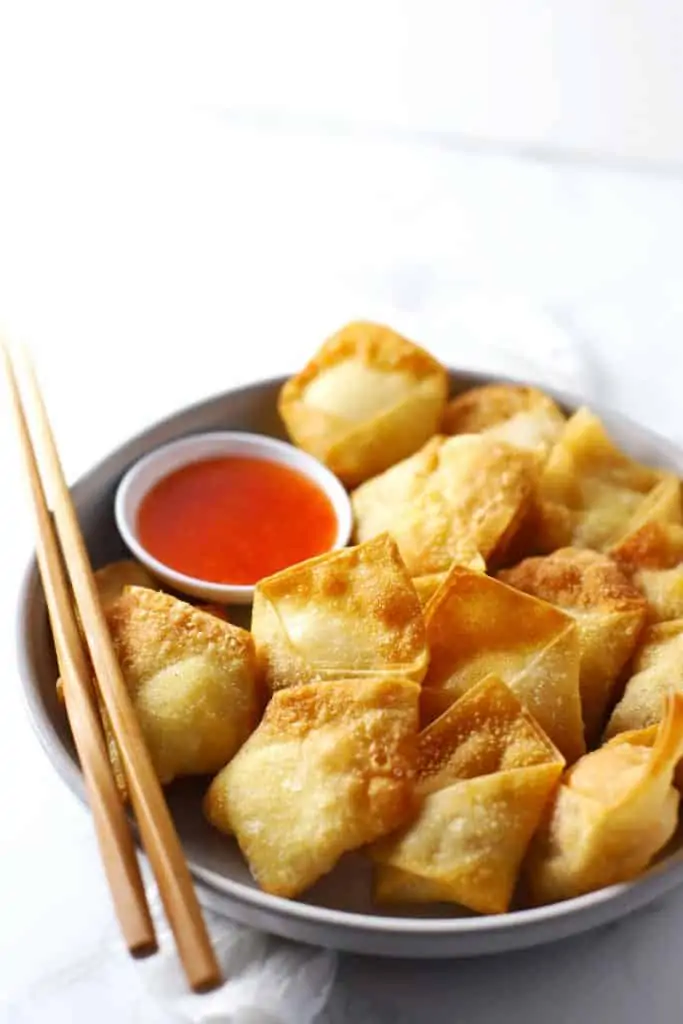 Cream cheese wontons on white plate with chopsticks. 