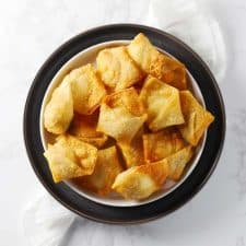 Cream cheese wontons on white and gray plates.