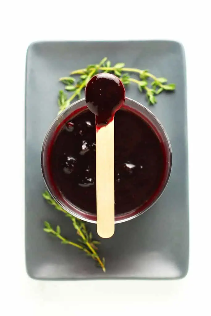 Blueberry lemon thyme sauce in glass bowl with wood spoon.