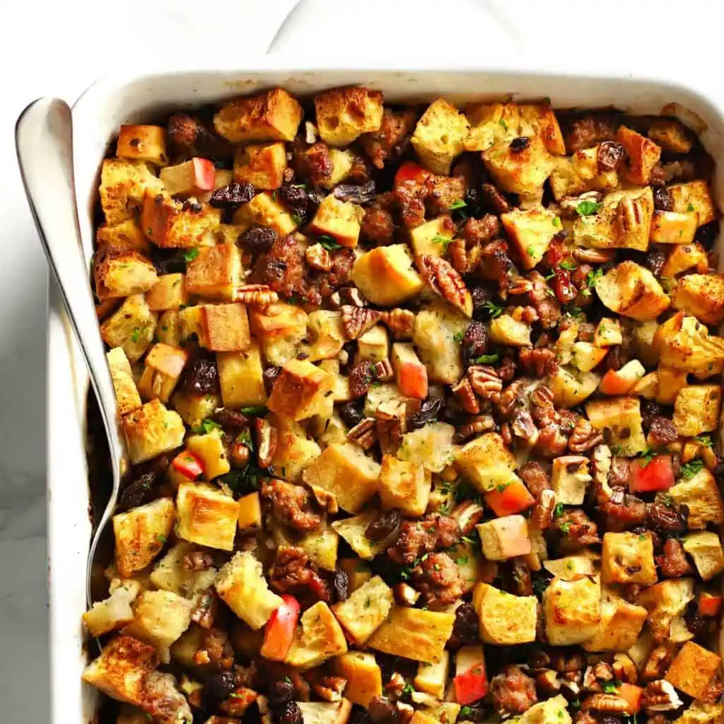 Italian sausage apple stuffing in white baking dish with serving spoon.