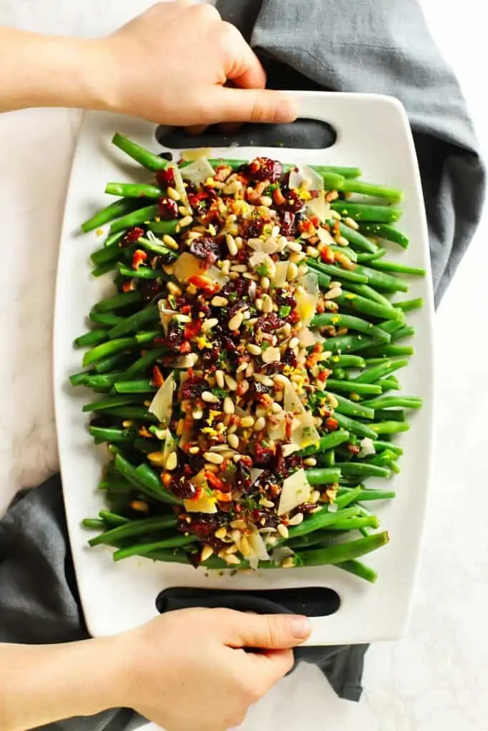 Two hands holding tray of lemon garlic green beans with crispy pancetta.