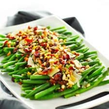 Lemon garlic green beans with crispy pancetta and loaded toppings on white tray with gray napkin.