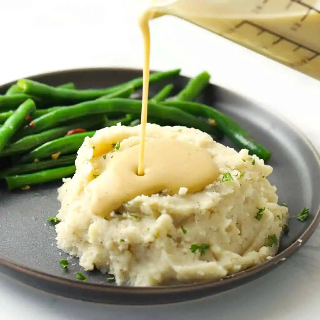 Pouring gravy on mashed potatoes.