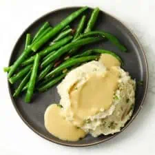 Mashed potatoes and gravy with green beans on grey plate.