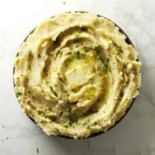 Mashed potatoes in grey bowl with butter and parsley.