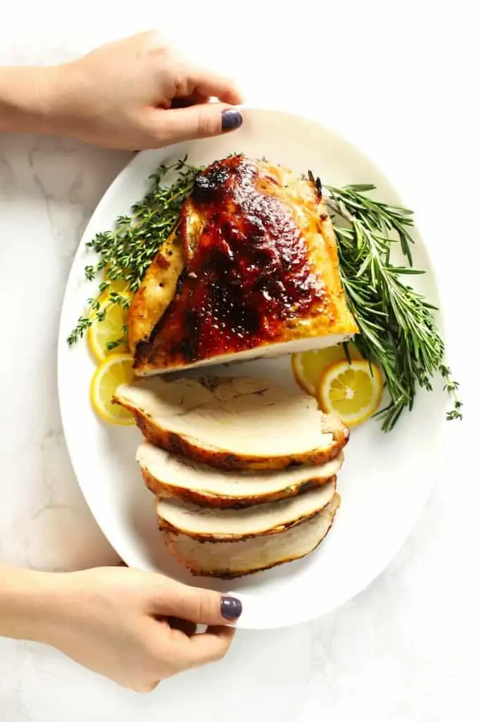 Two hands holding white platter with sliced roasted boneless turkey breast.