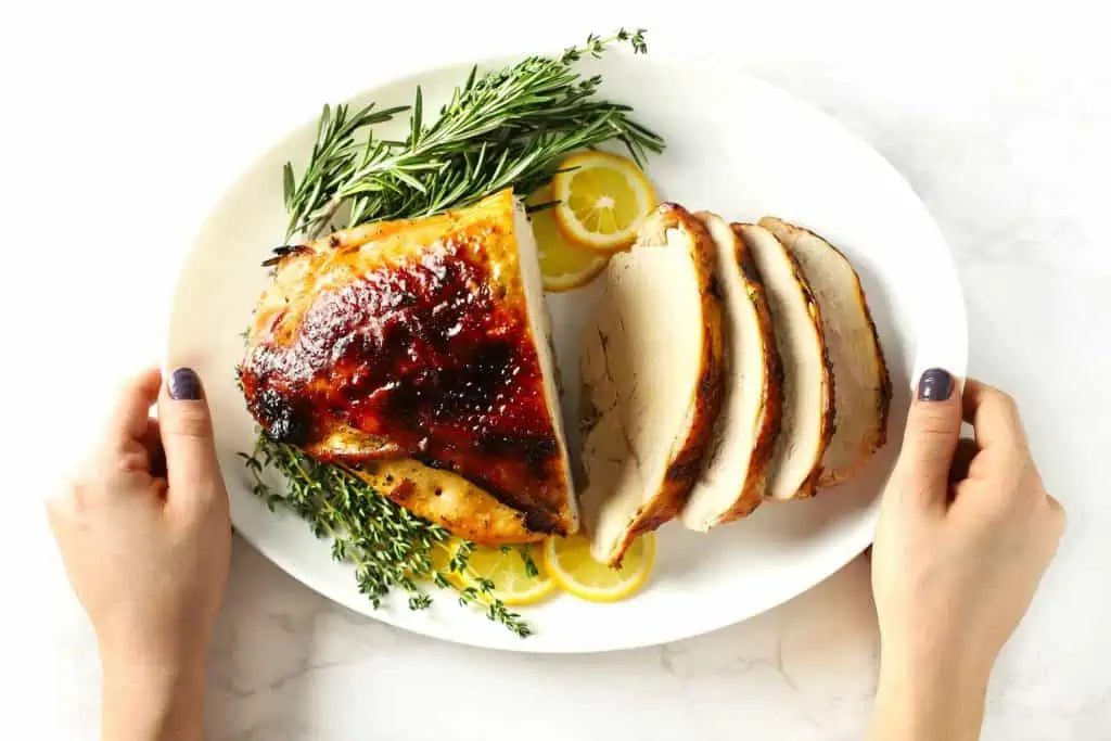 Two hands holding white platter with sliced roasted boneless turkey breast.