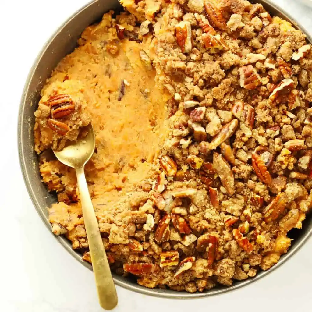 Sweet potato casserole in grey bowl with brass spoon.