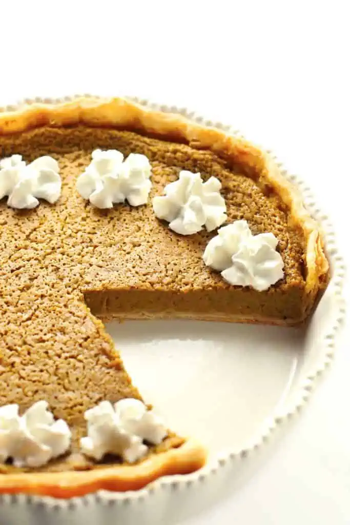 Pumpkin pie in white dish with whipped cream.