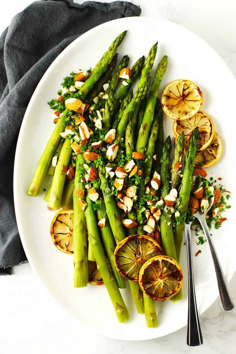 Baked asparagus on white platter with lemon and almonds. 