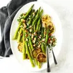Baked asparagus on white platter with lemon and almonds.