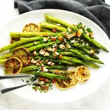 Baked asparagus on white platter with almonds and lemon.