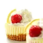 A mini cheesecake with whipped cream, a raspberry and a lemon slice.