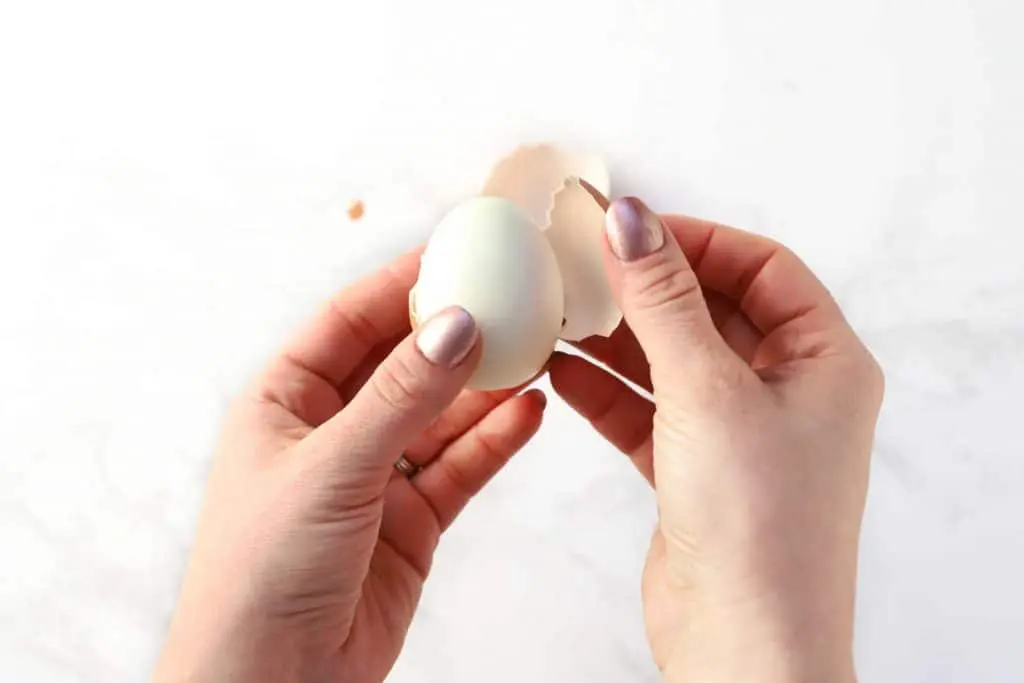 Two hands peeling a hard-boiled egg.