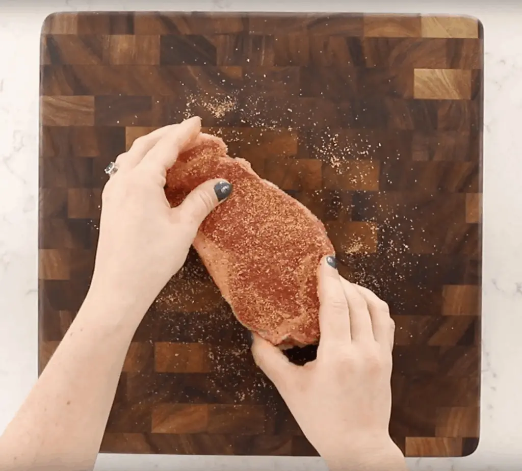 Steak on cutting board with seasoning.