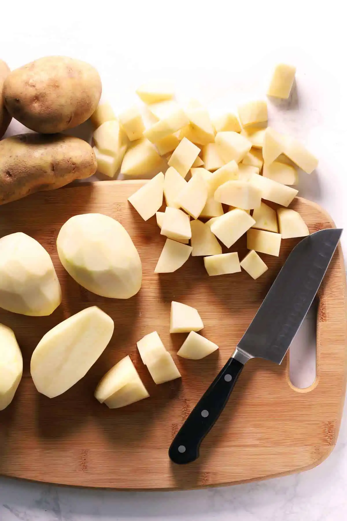 Peeled and cubed russet potatoes on cutting board with knife. 