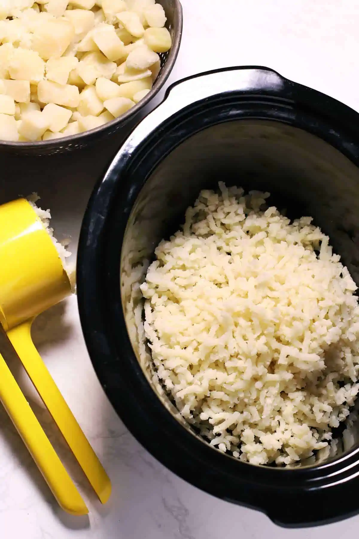 Mashing potatoes with ricer in a slow cooker. 
