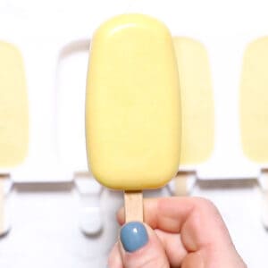 A coconut mango popsicle with popsicle mold in the background.