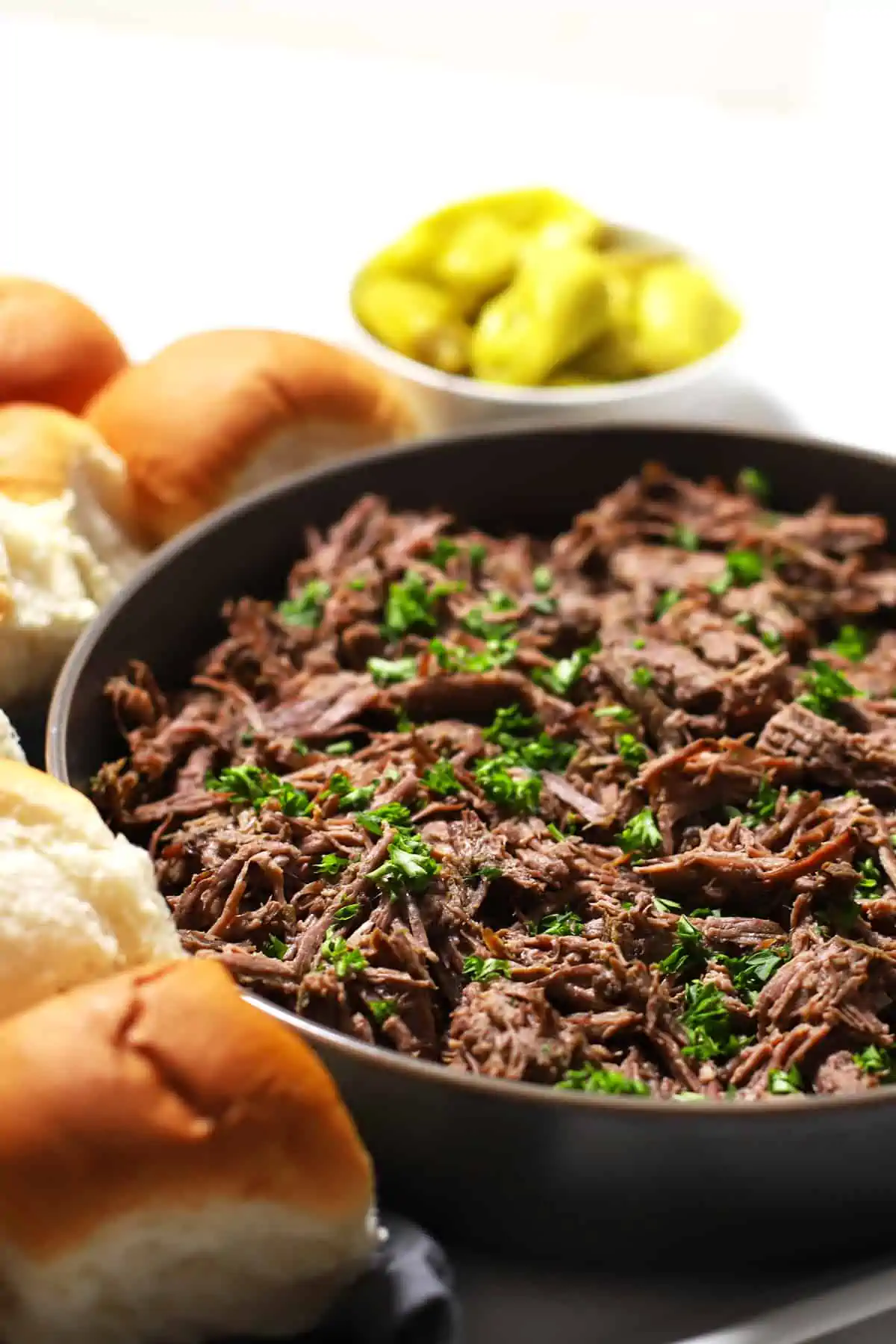 Shredded Italian beef on grey bowl on a platter with rolls. 