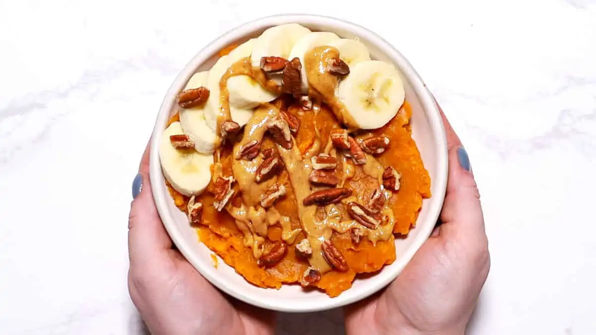 Two hands holding a Peanut Butter Banana Sweet Potato Breakfast Bowl. 