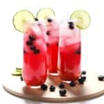 Three blueberry margaritas on a natural wood tray.