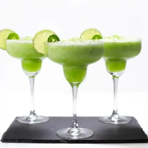Three frozen margaritas with lime and jalapeno slices.