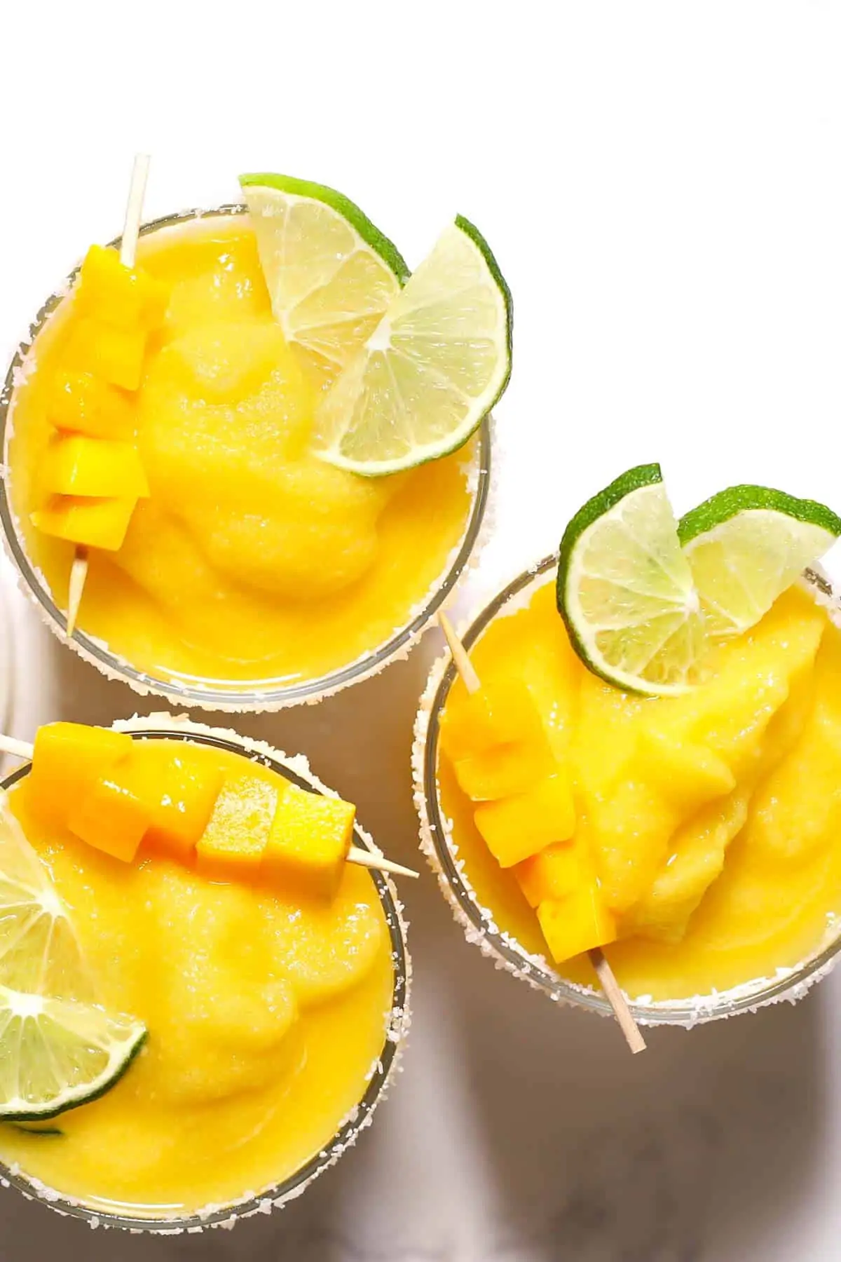 Frozen mango margaritas garnished with lime and fresh mango. 