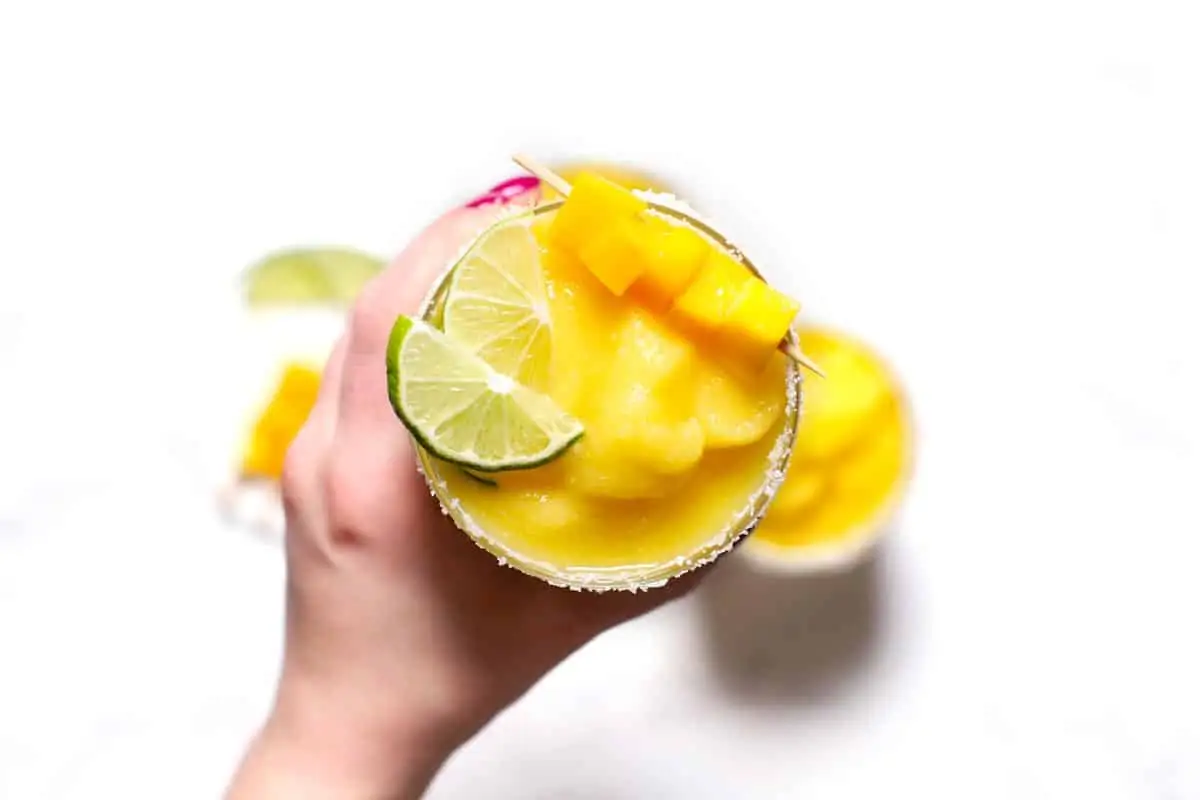 A hand holding a frozen mango margarita. 